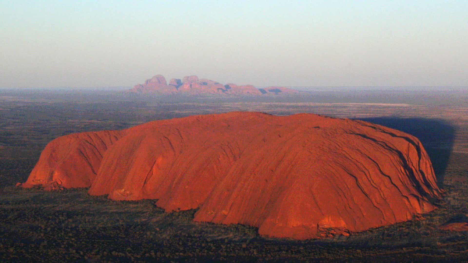 Visit Australia for: The red beauty of Uluru in the Outback seen from the air with Kata Tjuta in the distance