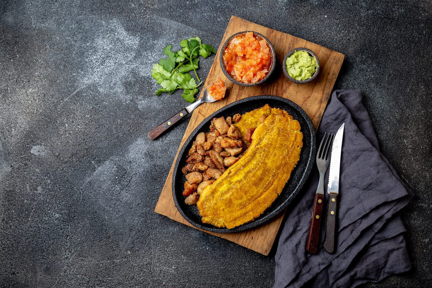 Colombian Caribbean Central American Food. Patacon Or Toston, Fried And Flattened Whole Green Plantain Banana On White Plate With Tomato Sauce And Chicharron Black Background, Top View